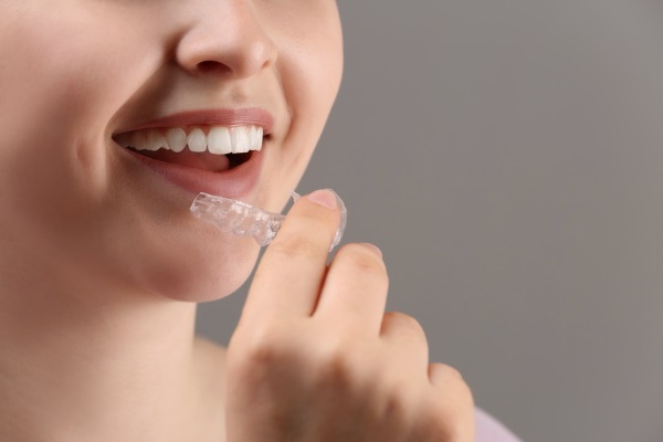 Woman putting occlusal splint in mouth on grey background, closeup